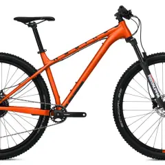 Pomarańczowy rower górski z amortyzatorem z przodu. Czy to hardtail czy full? Ten model to hardtail, idealny na podjazdy i zjazdy.