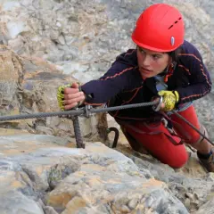 Młoda kobieta w kasku wspina się po skale, używając liny na via ferrata Czechy.