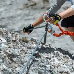 Ręce w rękawiczkach z karabinkami zabezpieczają się na stalowej linie podczas wspinaczki. To przygoda na via ferrata Słowacja.