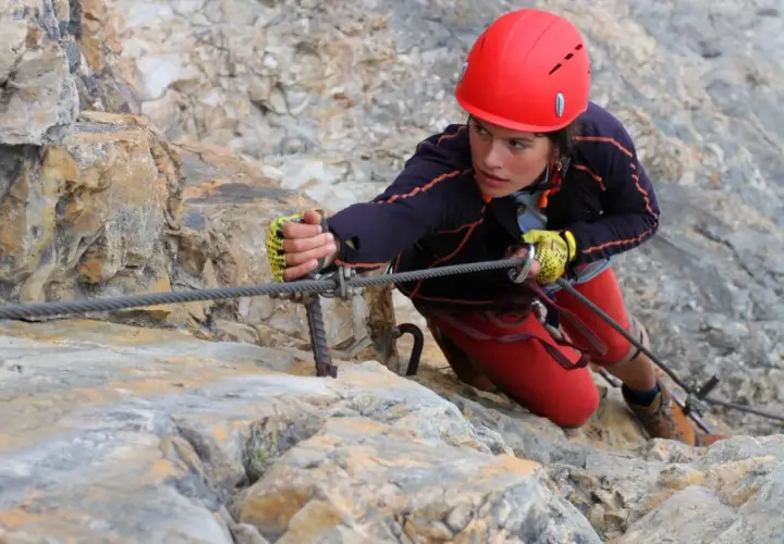 Młoda kobieta w kasku wspina się po skale, używając liny na via ferrata Czechy.