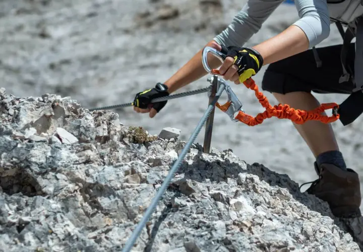 Ręce w rękawiczkach z karabinkami zabezpieczają się na stalowej linie podczas wspinaczki. To przygoda na via ferrata Słowacja.