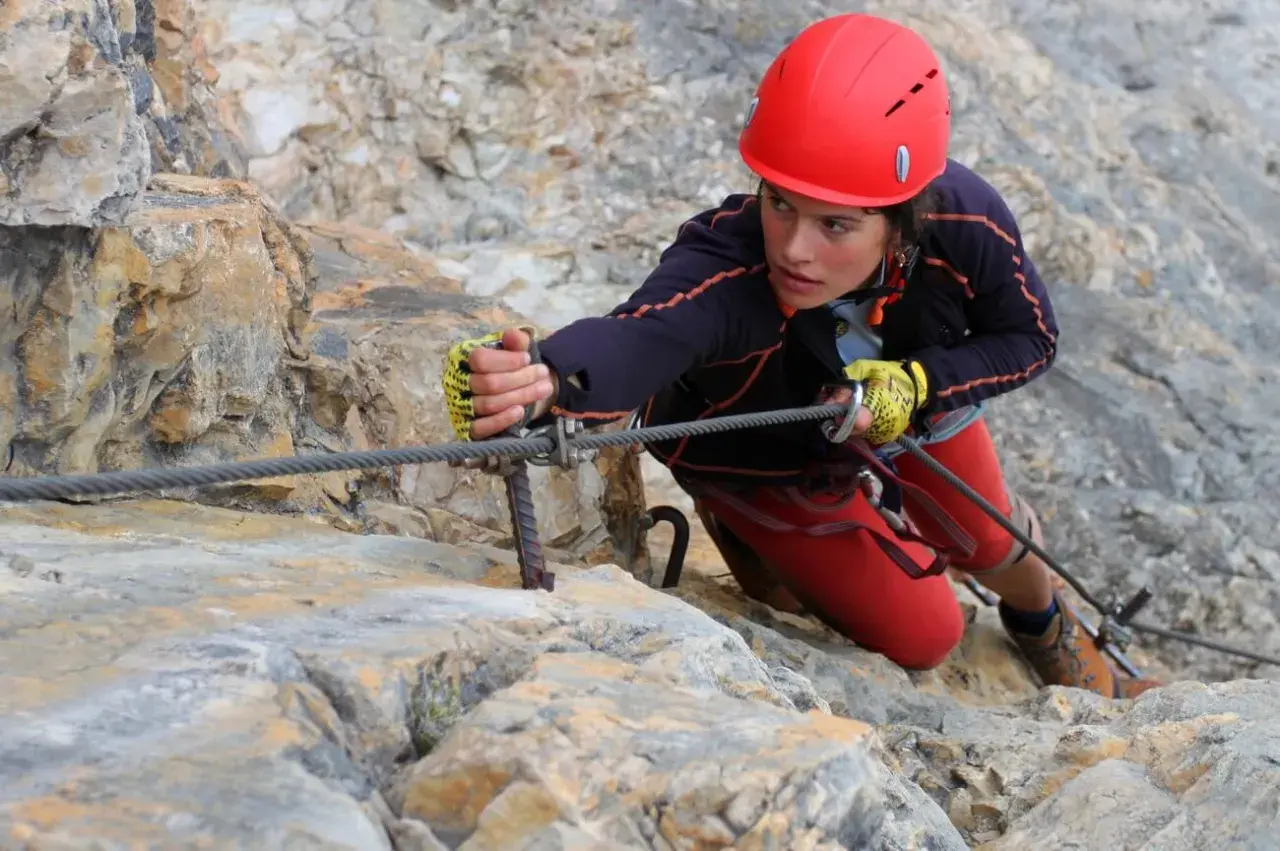 Młoda kobieta w kasku wspina się po skale, używając liny na via ferrata Czechy.