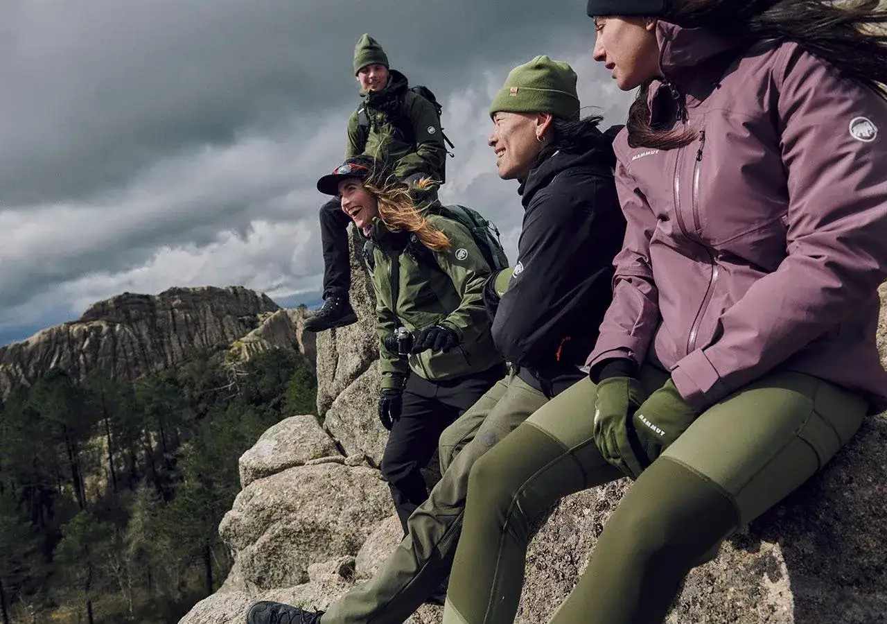 Grupa przyjaciół w zielonych czapkach i kurtkach, podziwiająca widok. Jaki softshell sprawdzi się w górach? Ten wygląda idealnie!